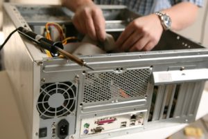 Person assembling or repairing a desktop computer, with hands inside the open case and various cables visible; a soldering iron is placed nearby.