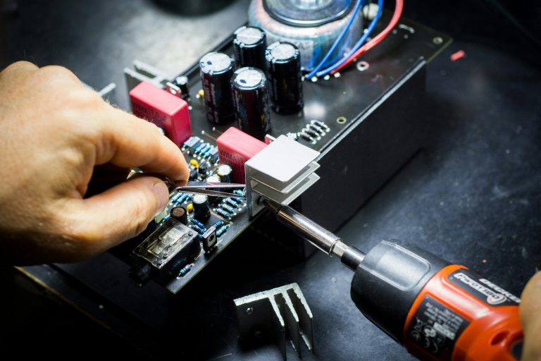 A close-up of a person using tools to repair an electronic circuit board with various components