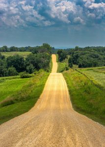 A long shot of a country road with grass fields on either side.