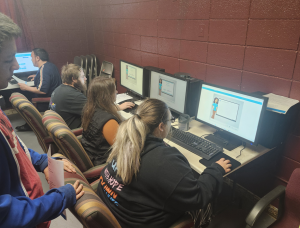 Several people sit at computers in a classroom, working individually on digital lessons displayed on their screens