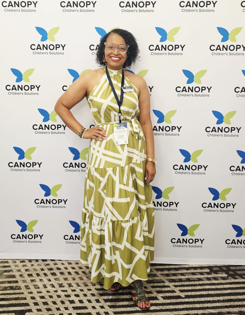 Canopy Children’s Solutions staff member smiles while standing in front of a branded Canopy event backdrop.