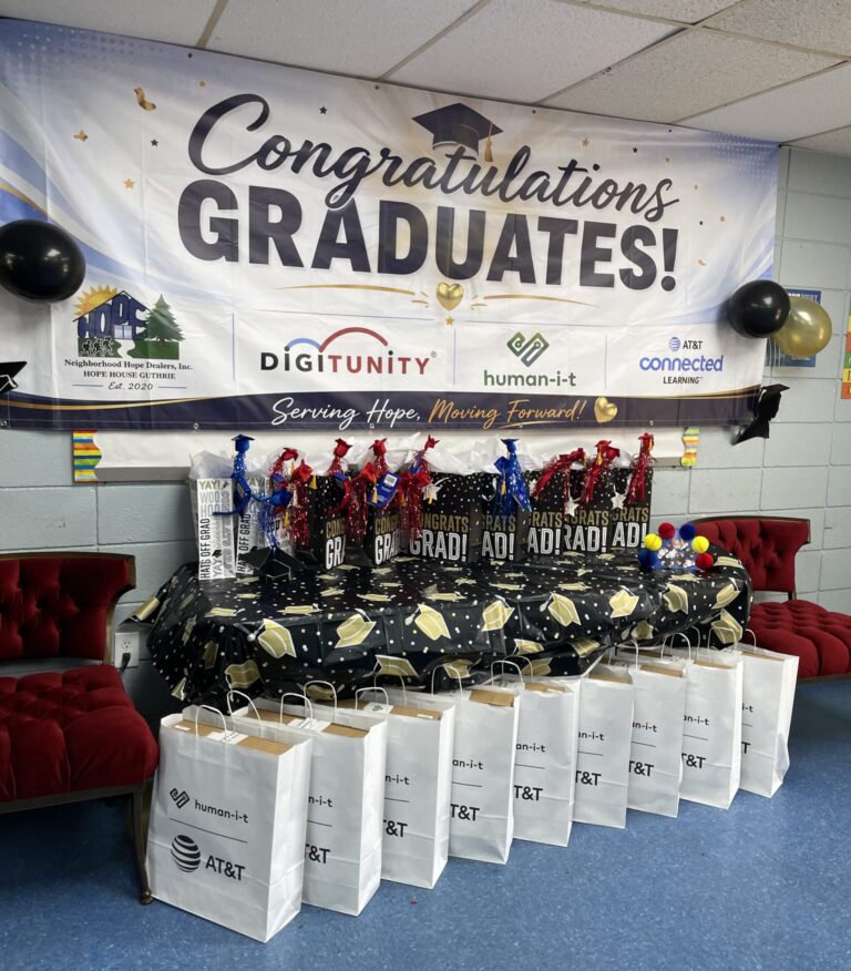 Graduation celebration setup with a “Congratulations Graduates!” banner featuring Neighborhood Hope Dealers, Digitunity, Human-I-T, and AT&T Connected Learning logos, with gift bags and graduation-themed decorations displayed below.