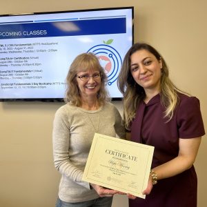 Two women standing in front of a screen, smiling and holding a certificate.