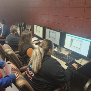 Several people sit at computers in a classroom, working individually on digital lessons displayed on their screens