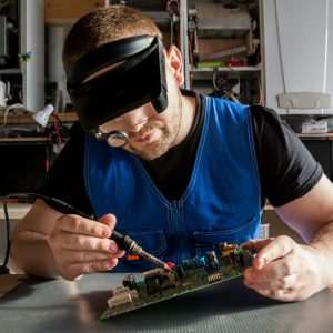 Person wearing goggles repairing a laptop hard drive.