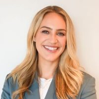kendra_shultz_headshot_720 A woman with long blonde hair wearing a light gray blazer and white top smiles at the camera against a plain light background.